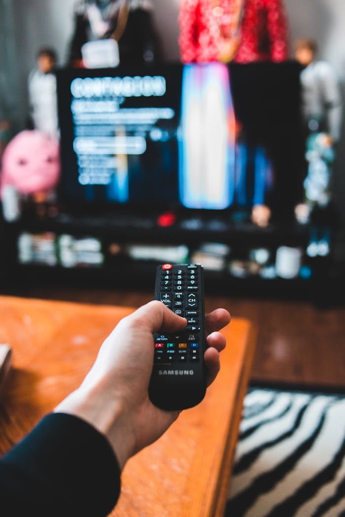 Person using a Samsung remote control in a living room setting for a relaxed movie night experience.